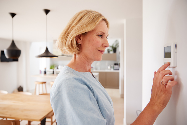 Close Up Of Mature Woman Adjusting Temperature At Home On Thermostat